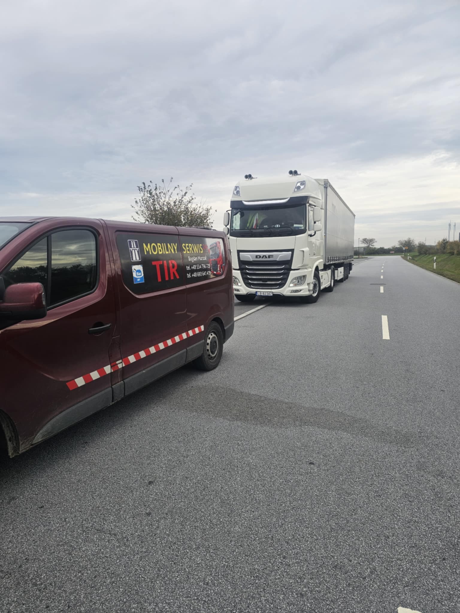 Samochód firmowy stojący przed ciężarówką na drodze.