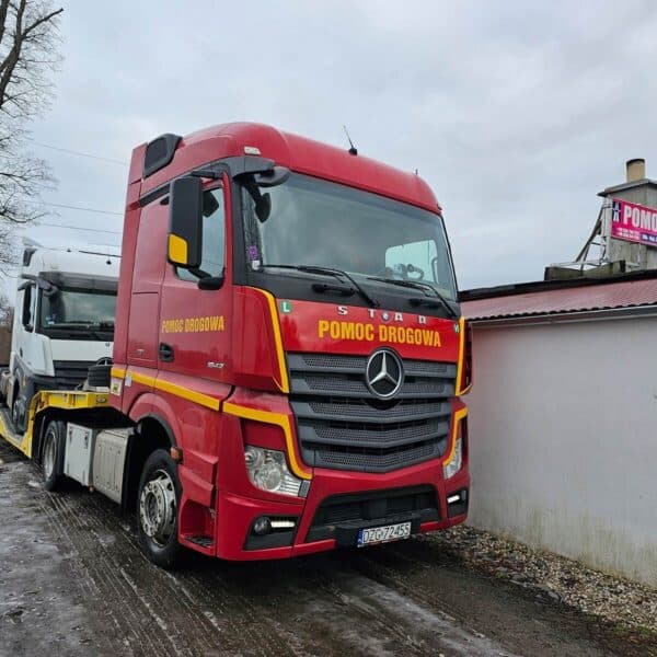 Biała ciężarówka na lawecie. Bliżej widać czerwoną ciężarówkę.